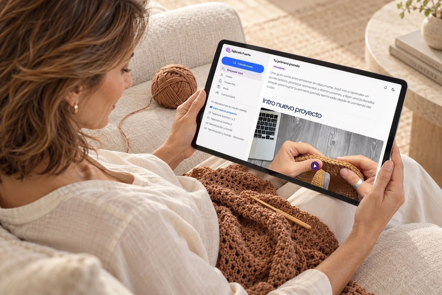 Escena editorial ilustrativa de una mujer en un sofá, con un proyecto de crochet y un ovillo, siguiendo una clase de Tejiendo Fuerte en su tablet.